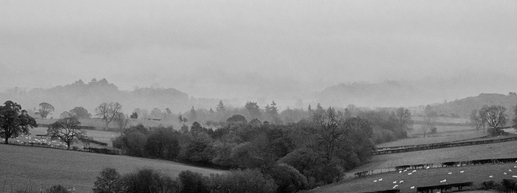 A black and white photograph of rolling hills of Wales in mist